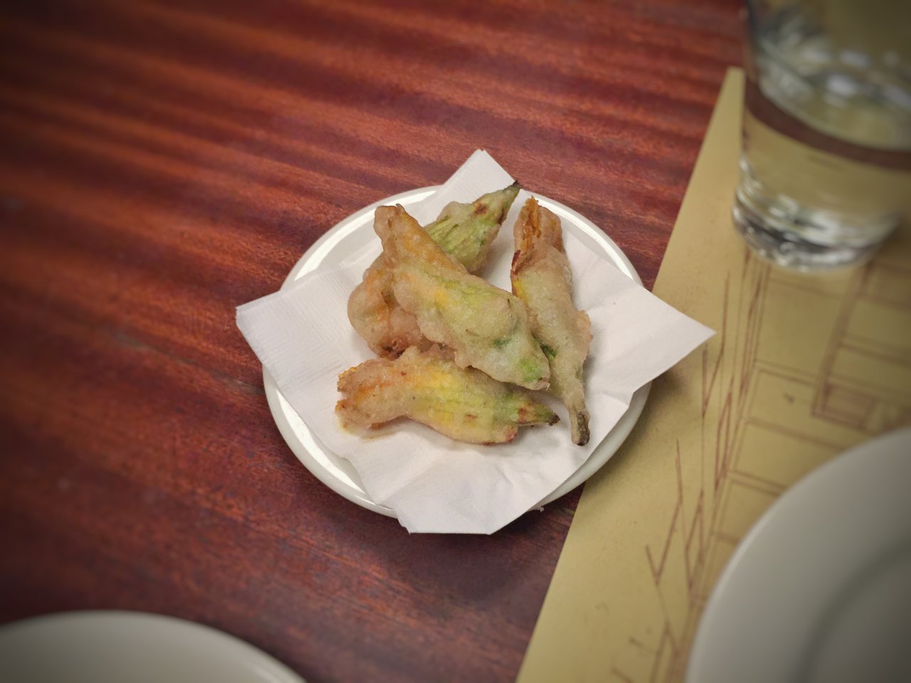 Beignets de fleurs de courgette (Cucurbita pepo) farcis à la ricotta, dorés en tempura, sur assiette blanche, préparation signature niçoise et liguro-italienne illustrant le mode culinaire beignet.