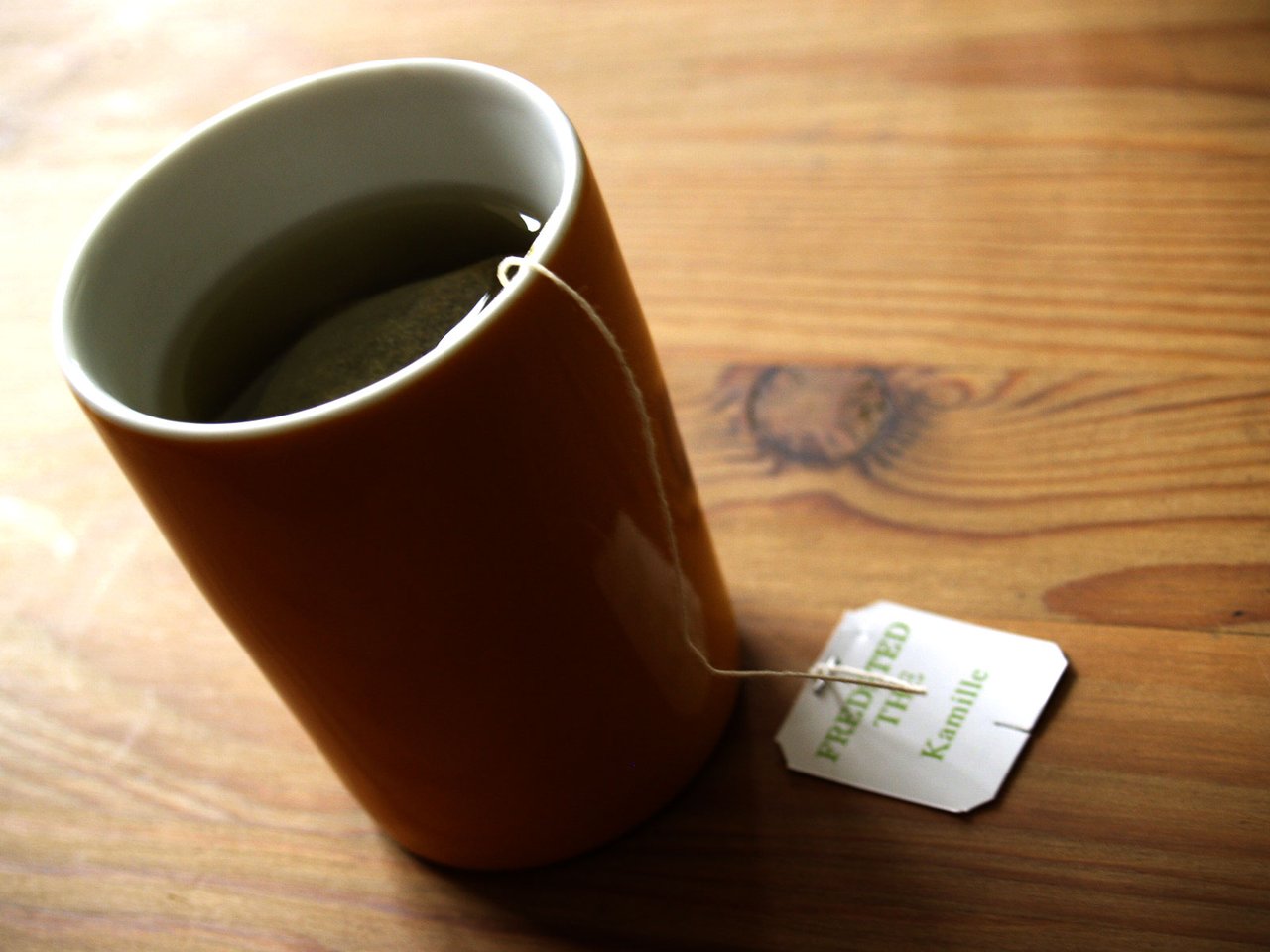 Tasse en verre transparent remplie d'une infusion ambrée de camomille, posée sur un plan de travail neutre