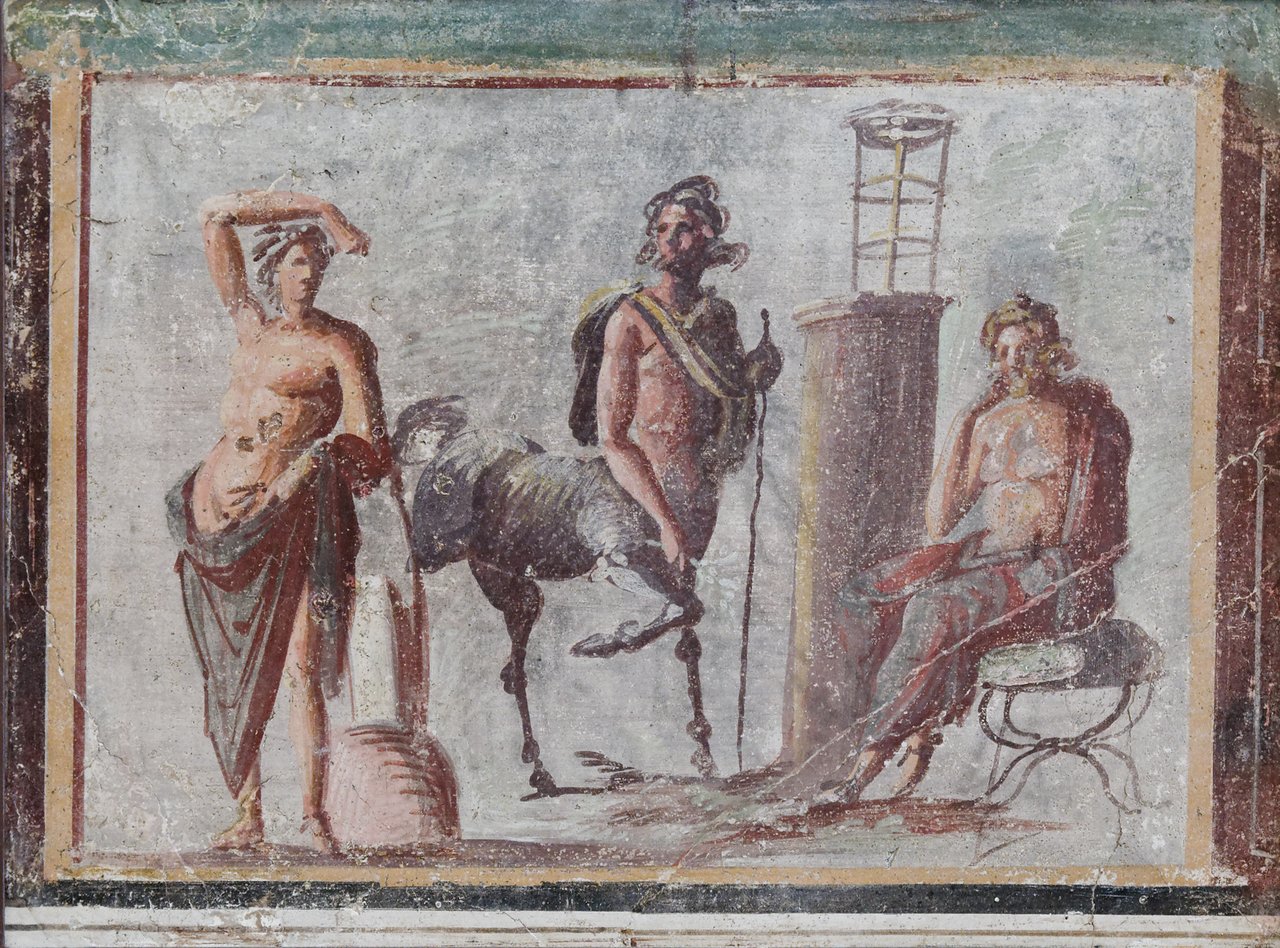 Fresque romaine du Iᵉʳ siècle apr. J.-C. provenant de Pompéi : Apollon, le centaure Chiron et Asclépios, scène mythologique fondatrice qui donne au genre Centaurea son nom grec kentauros, en référence aux vertus médicinales que Chiron aurait découvertes dans la fleur
